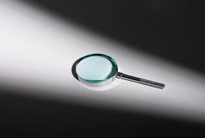 Silver magnifying glass on glass surface, shadow and light play. Optical zoom lens concept, photo