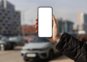 Hand showing mobile phone screen mockup, city background, car photo