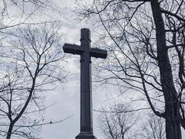 Religious cross over overcast gloomy sky with bare trees, creepy mood photo