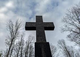 Religious cross over overcast sky with bare trees, gloomy mood, bottom view photo