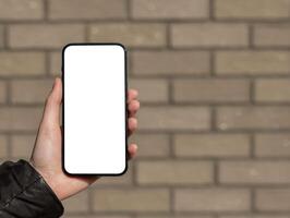 Hand showing mobile phone mockup, smartphone screen, brick wall background photo