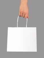Hand holding shopping bag, paper packet, pack with handles, white package isolated photo
