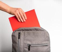 Hand taking red book, textbook from backpack, schoolbag photo