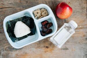 cena en un musulmán caja de almuerzo en un asiático país de onigiri, manzana y soja salsa con un botella de agua foto