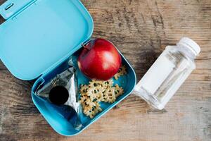 asiático estudiantes caja de almuerzo de onigiri, patatas fritas y manzana con botella de agua, en de madera antecedentes foto