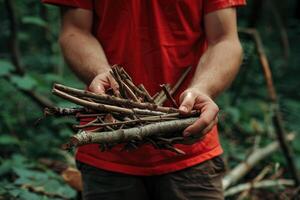 Man in red shirt collects sticks for campfire in forest. photo