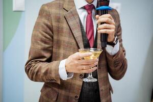 un mano sostiene un vaso de champán, un martini es vertido dentro un vaso, un hombre dice un brindis dentro un micrófono, un negocio hombre en un chaqueta, un fiesta, un evento presentación. foto