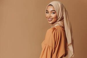 Stylish Muslim woman in beige outfit smiling on brown background. photo