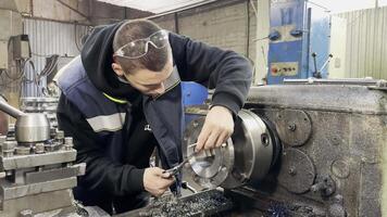 A young trainee employee measures a workpiece with a caliper on a lathe and screwcutting machine video