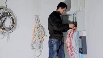 un eléctrico ingeniero conecta un eléctrico tablero de conmutadores en un nuevo hogar. el hombre ajusta el eléctrico panel y arregla el eléctrico alambres video