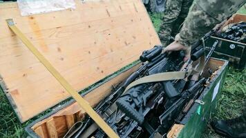 de leger zet kalashnikov aanval geweren en scherpschutter geweren in een doos. lossen van leger apparatuur. hand- dichtbij omhoog zet in een houten doos kalashnikov geweer- en scherpschutter geweer. video