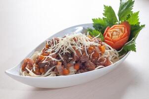 spaghetti bolognese with cheese sprinkled is placed on a white plate with a white background photo