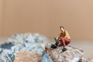 miniatura personas , un joven hombre bebiendo cerveza mientras sentado en el rock foto