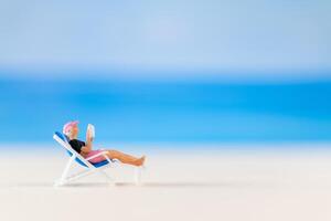 Miniature people , a woman relaxing on a deck chair and reading a book photo