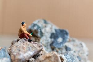 miniatura personas , un joven hombre bebiendo cerveza mientras sentado en el rock foto