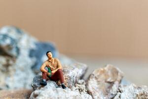 Miniature people , A young man sipping beer while sitting on the rock photo