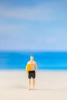 miniatura personas hombre en un traje de baño, y participación un amarillo tabla de surf en el playa foto