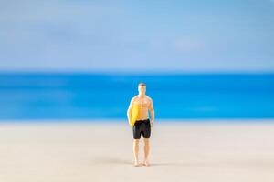 miniatura personas hombre en un traje de baño, y participación un amarillo tabla de surf en el playa foto