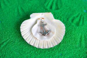 Jewelry anchor pendant from silver with seashells on an artificial green sand. Handcraft precious item. Sea theme. photo