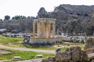 Ancient Greek temple ruins with tall stone columns and intricate carvings on capitals. Large flat stone platform with scattered pieces. Historical architecture marvel. photo