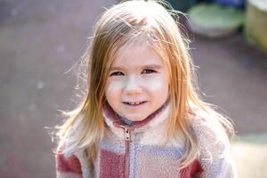 sonriente joven niña vistiendo un elegante a cuadros chaqueta, posando para el cámara con un borroso al aire libre antecedentes de arboles ella exuda alegría y felicidad en el natural ajuste. foto