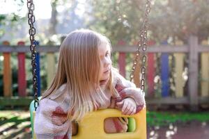 Little girl on a swing looking away, thoughtful expression, retro colors. photo