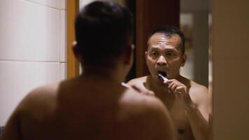 Asian man brushing his teeth in the bathroom. Morning routine activities. video