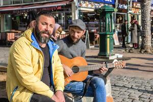 Istanbul, Turkey - December 29, 2022. Two men are sitting on bench by the street and one of them playing guitar. photo