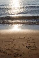 Drawing sun on a sandy beach near to sea. The symbol of resting in sunny day on vacation rest. photo