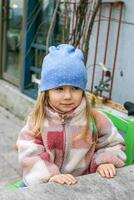 A young girl with blonde hair smiles in a blue hat with white polka dots, a colorful jacket, and white and pink gloves. Isolated on a red background, the image exudes joy. photo