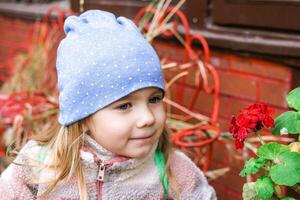 joven niña admirativo un vibrante rojo flor en un hermosa jardín ajuste. foto