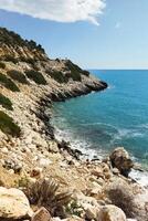 A picturesque rocky beach in the Mediterranean Sea with clear blue water and stones. The beach is in a cove surrounded by cliffs. Crystal clear water allows you to see the stones on the seabed. photo