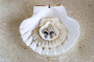 Pair of silver earrings on a background of seashells and sand. Handcraft precious item. Sea theme. photo