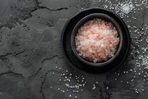 A bowl of pink salt is on a grey surface photo