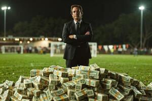 Confident businessman with pile of money on soccer field photo