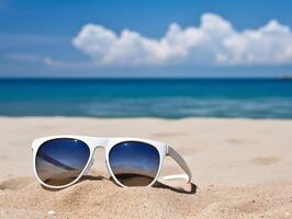 blanco Gafas de sol descansando en un arenoso playa con claro azul Oceano antecedentes. verano vacaciones concepto foto