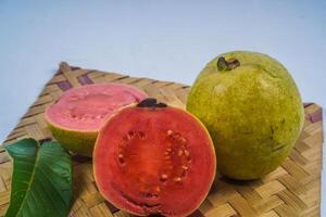 Guava isolated. Collection of red fleshed guava fruit with yellowish green skin and leaves isolated on a white background with bamboo matting. photo