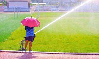 trabajador utilizando grande pistola alto presión aspersor a riego césped campo en grande fútbol estadio foto