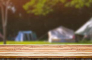 Blank wooden table top on blurred background of camping tents in campground area at nature parkland for montage mockup product display in travel and recreation or leisure activity concept photo