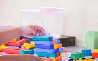Close up image of child hands is playing colorful wooden blocks toy on table at home or kindergarten photo