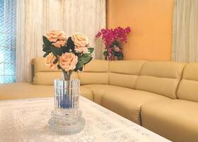 Selective focus at beautiful artificial roses bouquet in crystal vase on a table covered with lace tablecloth with beige sofa in modern living room photo