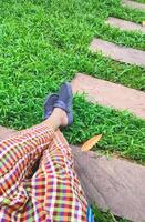 Part of man's legs in colorful plaid trousers with cross-legged gesture resting on bench in rest area at public park, top view with copy space photo