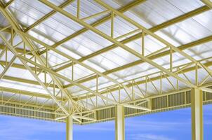 Low angle and perspective side view of yellow metal building roof structure with heat insulations in construction site area with blue sky background photo