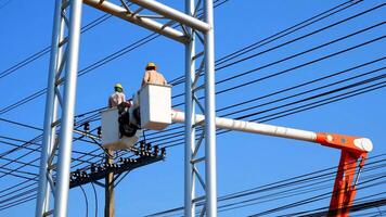 Two electricians on bucket boom truck are installing electrical system on power pole against blue clear sky background photo