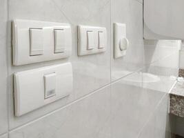 Side view and selective focus at light switches with fan switch and part of air hand dryer on white tile wall in public restroom area photo