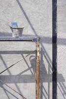 Cement bucket with plastering tools on scaffolding with sunlight and shadow on concrete wall surface inside of house construction site in vertical frame photo