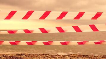 Red white warning tape barrier ribbon swinging in the wind across exotic sea beach background without people. No entry Red White caution tape. No holiday concept, delayed travel, no summer plans video