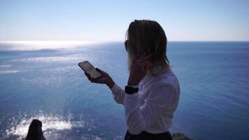 Business woman talking by phone on the sea. Digital nomad, Pretty lady typing on computer by the sea at sunset, makes a business transaction online from a distance. Freelance, remote work on vacation video