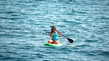 hav kvinna supera. silhuett av Lycklig positiv ung kvinna i blå bikini, surfing på grön supera styrelse genom lugna vatten yta. idyllisk solnedgång. aktiva livsstil på hav eller flod. långsam rörelse video