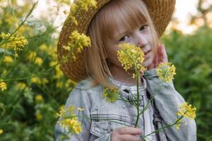 Blonde girl in a field with yellow flowers. A girl in a straw hat is picking flowers in a field. A field with rapeseed. photo